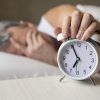 Man lying in bed turning off an alarm clock in the morning at 7a